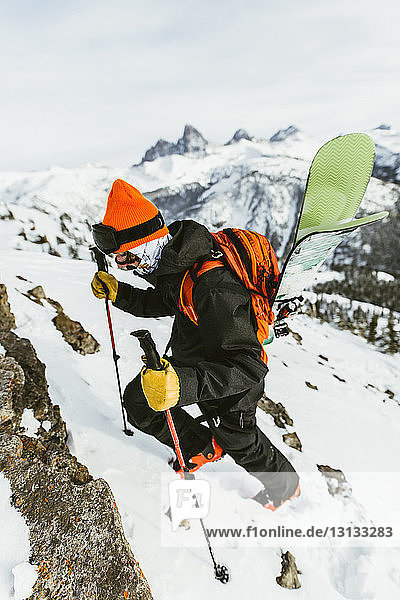 Wanderer mit Rucksack und Skistöcken besteigt schneebedeckten Berg