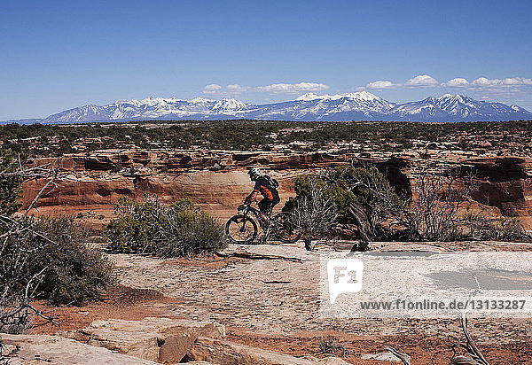 Side view of man cycling on rocks against sky