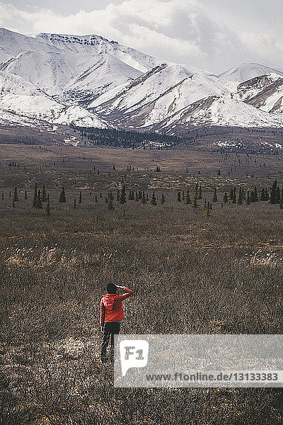 Rear view of woman standing on field against snowcapped mountains at Denali National Park