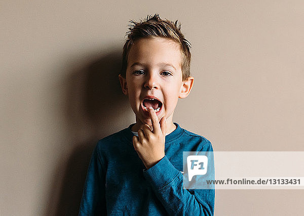 Portrait of boy touching teeth while standing against wall at home