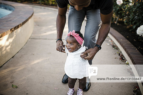 Vater hilft glücklicher Tochter beim Gehen auf Fußweg im Park