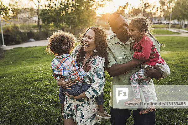 Fröhliche Eltern tragen Kinder bei Sonnenuntergang auf dem Feld im Park