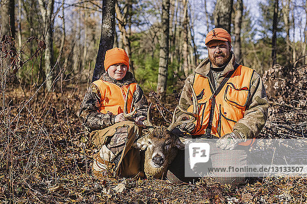 Portrait of father and daughter with dead deer on field during hunting