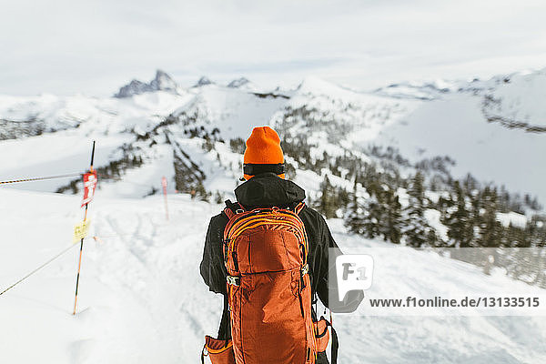 Rückansicht eines Wanderers mit Rucksack auf einem schneebedeckten Berg während eines Skiurlaubs