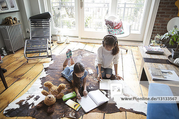 High angle view of sisters relaxing on carpet and studying at home