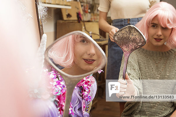 Woman wearing pink wig while looking at hand mirror in clothing store