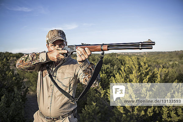 Hunter aiming with rifle while standing against sky