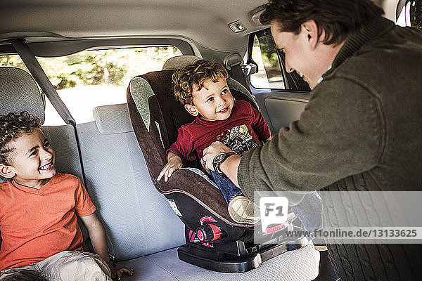 Vater setzt Sohn auf Kindersitz im Auto