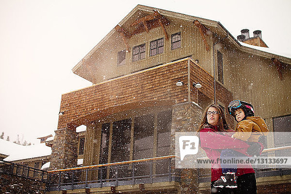 Mutter  die einen Sohn trägt  während sie bei Schneefall vor einem Touristenort steht