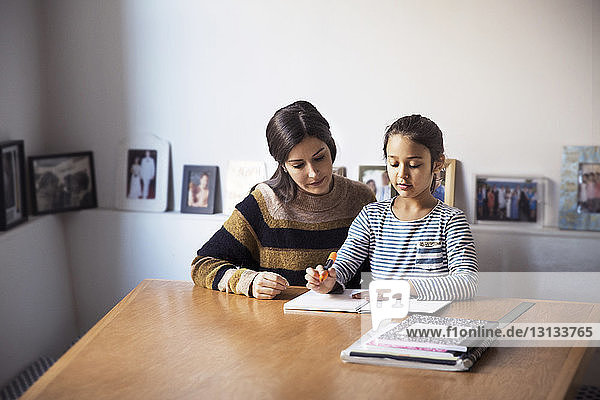 Mutter hilft Tochter beim Lernen  während sie am Tisch sitzt