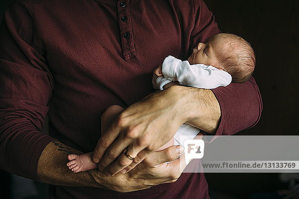 Midsection of father carrying cute sleeping daughter at home