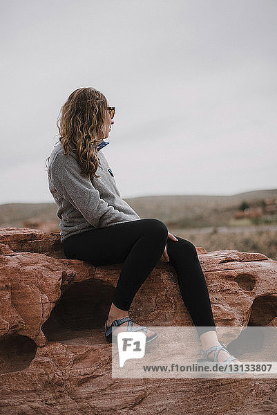 Frau in voller Länge sitzt auf Felsen gegen den Himmel in der Red Rock Canyon National Conservation Area