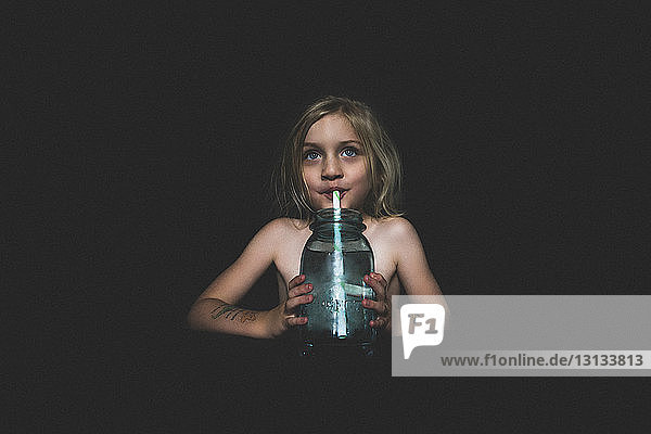 Shirtless girl drinking juice while sitting in darkroom at home