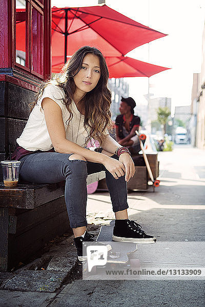 Porträt einer jungen Frau  die mit einem Skateboard auf einer Stützmauer sitzt
