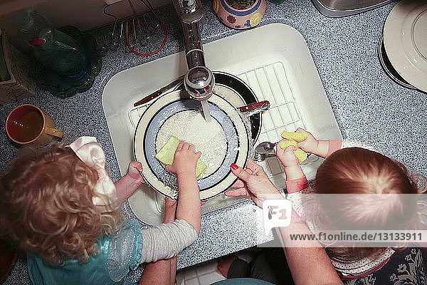 Cropped hands of grandmother with grandchildren washing plates in kitchen