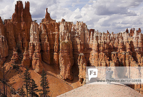 Man photographing hoodoos while crouching on rock