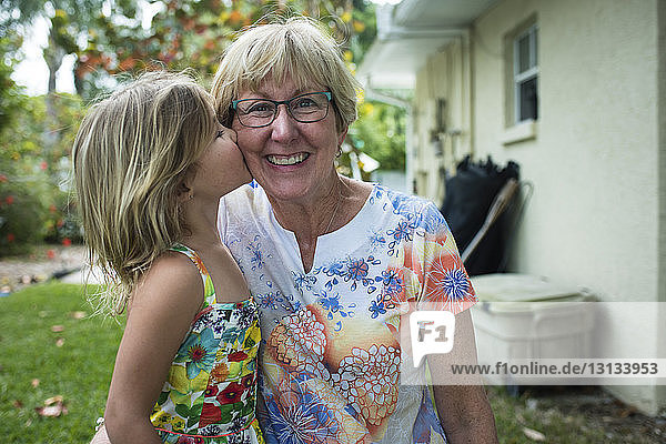 Porträt einer fröhlichen Großmutter mit Enkelin  die sie im Hof küsst