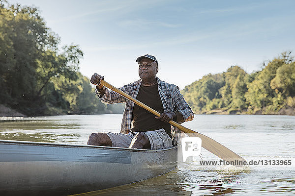 Mature man looking away while rowing on lake against sky