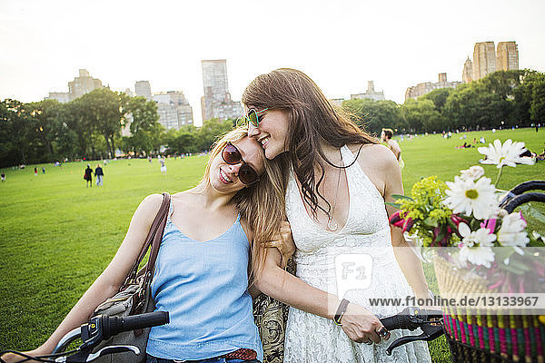 Smiling romantic lesbian couple with bicycles on grassy field at park