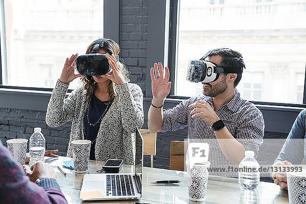 Colleagues wearing virtual reality simulator while sitting in office