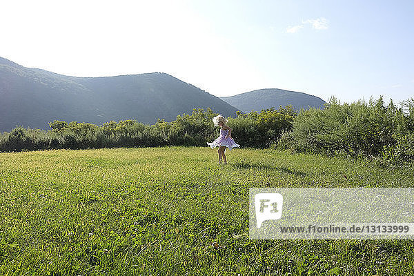 Playful girl spinning on grassy field against mountains and sky