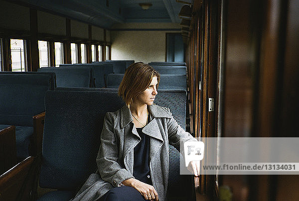 Thoughtful woman looking through window while sitting in train