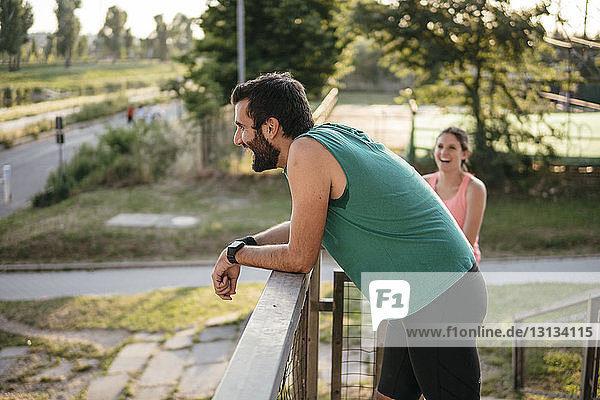 Happy man looking away while exercising at park with woman in background