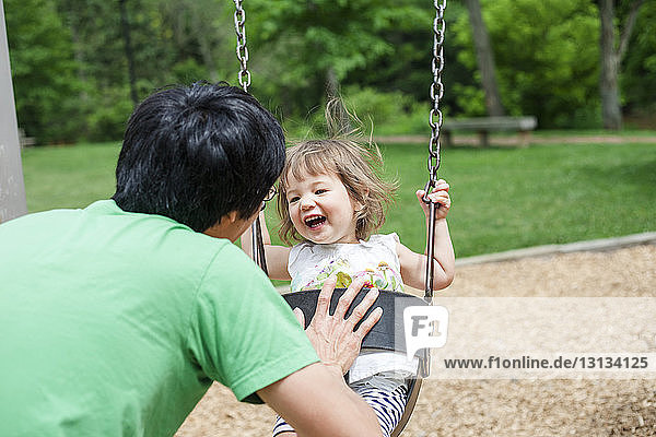 Rückansicht eines Vaters  der seine glückliche Tochter auf dem Spielplatz schubst