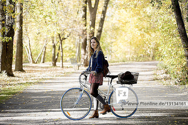 Bildnis einer Frau mit Fahrrad auf der Strasse inmitten von Bäumen stehend