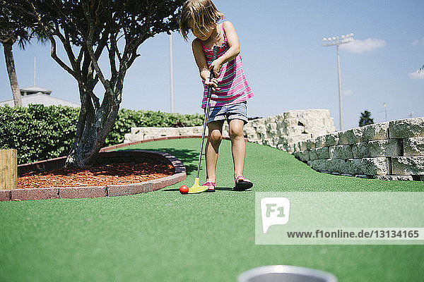 Mädchen spielt Minigolf an einem sonnigen Tag