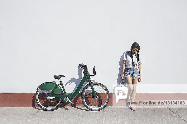 Junge Frau  die einen Helm hält  während sie mit dem Fahrrad auf dem Bürgersteig steht