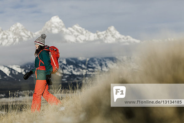 Seitenansicht einer Wanderin mit Rucksack vor schneebedeckten Bergen