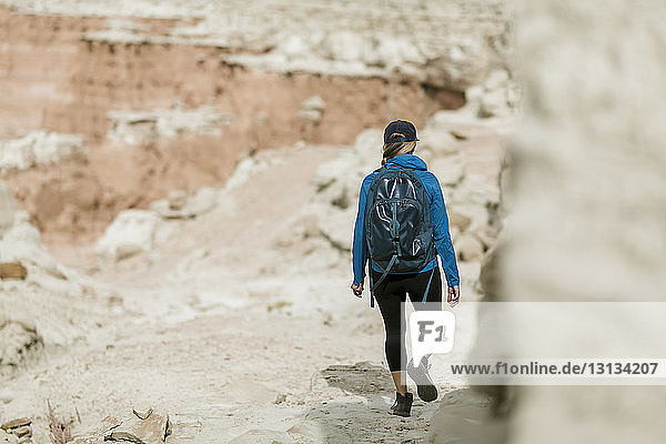 Rückansicht einer Wanderin mit Rucksack beim Wandern gegen Felsformationen in der Wüste
