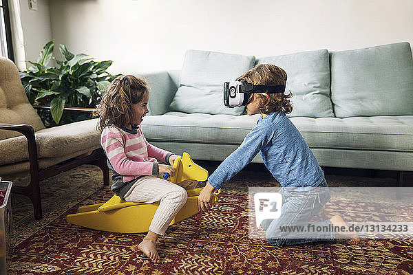 Boy wearing virtual reality simulator playing with sister sitting on rocking horse at home