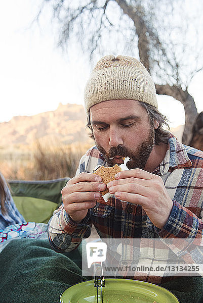 Mid adult man eating s'more at camp site