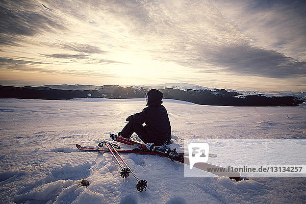 Rear view of skier sitting on snowy mountain against sky