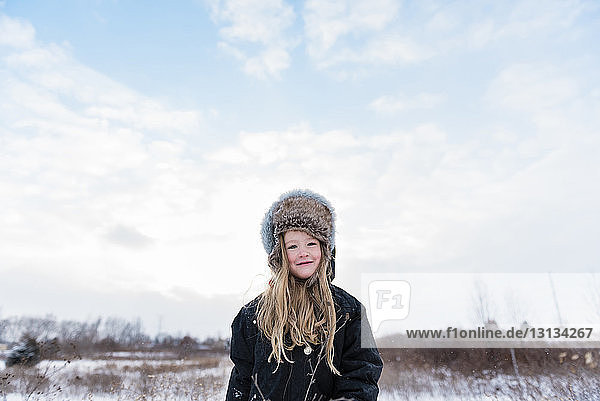Portrait of confident girl wearing warm clothing while standing against cloudy sky during winter