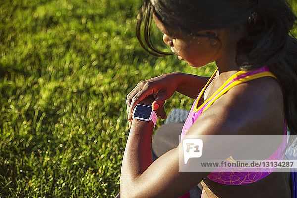 High angle view of female athlete checking wristwatch while crouching on grassy field