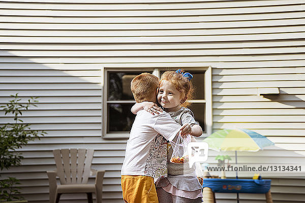 Süße Kinder umarmen sich  während sie Schokoladenbeutel gegen das Haus halten
