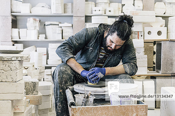 Craftsman using pottery wheel while making earthenware in workshop