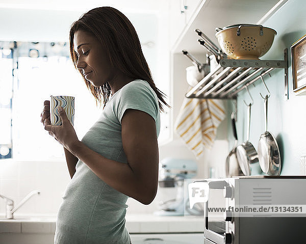 Lächelnde Frau hält Kaffeetasse  während sie an der Küchentheke steht