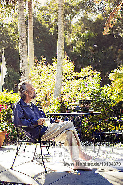 Thoughtful senior man sitting on chair in back yard