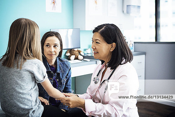 Smiling female doctor examining girl's hand in clinic