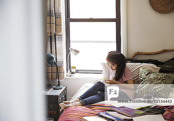 Teenagerin benutzt Smartphone  während sie auf dem Bett sitzt
