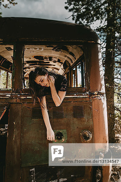 Young woman leaning out of abandoned bus's window