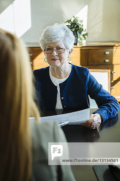 Ältere Frau hält Dokumente in der Hand  während sie mit dem amtierenden Finanzberater diskutiert