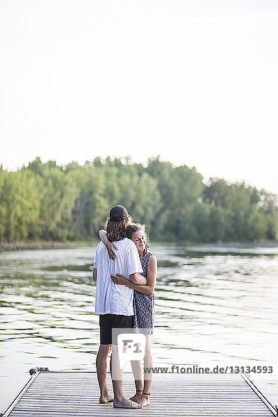 Paar umarmt sich  während es auf der Mole über dem See vor klarem Himmel steht
