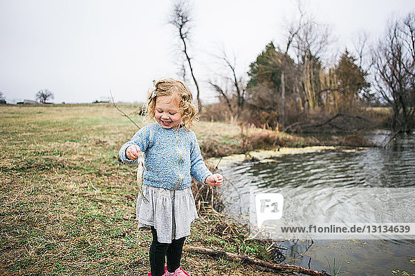 Cheerful girl holding fish while fishing by lake