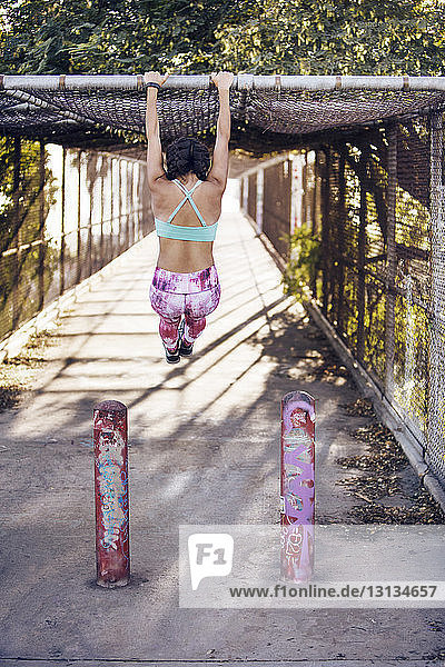 Rear view of woman exercising on bridge on sunny day