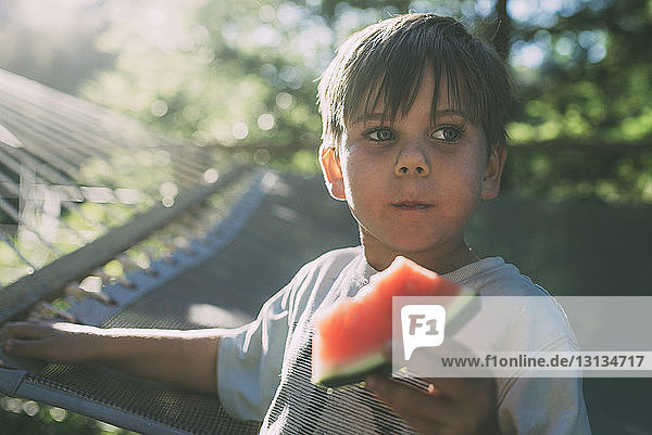 Junge isst Wassermelone gegen Hängematte an einem sonnigen Tag
